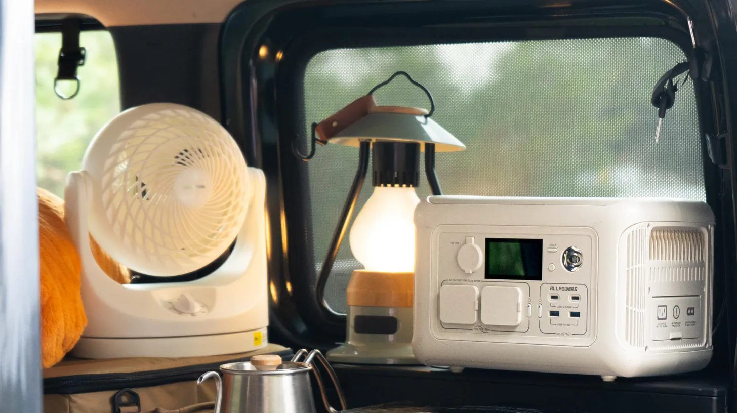 Station d'énergie portable ALLPOWERS dans un van aménagé, à côté d'un ventilateur et d'une lanterne de camping